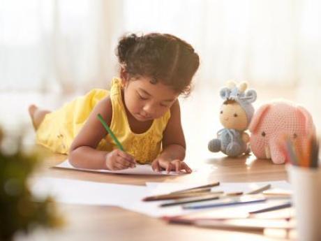 Young child lying on the floor and coloring pages with crayons
