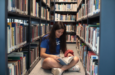 Girl sitting on library floor with an open book in her lap